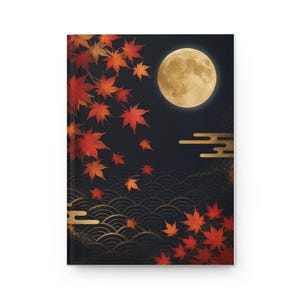 Pode incluir: Um caderno de capa dura com um fundo escuro e uma grande lua cheia brilhante. Folhas de bordo vermelho-brilhante e laranja estão espalhadas pela capa, acentuadas por padrões de ondas douradas e linhas horizontais.