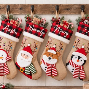 Könnte beinhalten: Vier Weihnachtsstrümpfe aus Jute hängen an einer Holzleiste. Jeder hat einen rot-schwarz karierten Umschlag mit den Namen Austin, Beverly, Merry und Emily. Die Strümpfe sind mit Plüschfiguren wie Schneemann, Weihnachtsmann, Hund und Pinguin verziert.