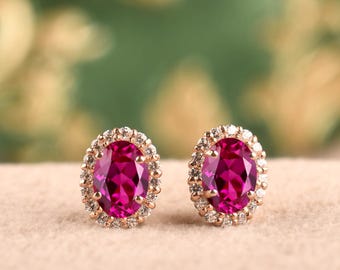 Peut inclure: Une paire de boucles d'oreilles à clous avec des pierres centrales ovales d'un rose éclatant. Chaque pierre précieuse est entourée d'un halo de petites pierres rondes transparentes serties dans une monture métallique, créant un bijou symétrique.