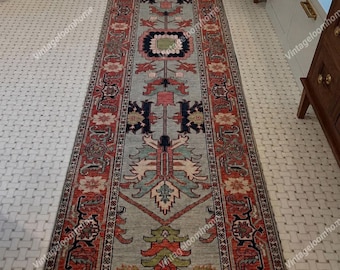 May include: A long rectangular runner rug featuring a light blue central field with intricate geometric and floral motifs in shades of red, navy blue, green, and cream. The border displays a repeating pattern in red and dark blue tones.