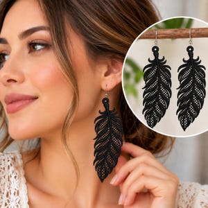 May include: A pair of matte black dangle earrings shaped like feathers. Each earring features a detailed, intricate lattice cutout pattern throughout the entire feather design, suspended from a simple silver-toned metal hook wire.