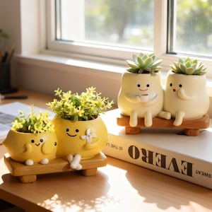 May include: Two sets of ceramic planters shaped like smiling characters sitting on wooden benches. One set features yellow lemon-like figures with green plants, while the other features cream-colored figures holding a cup and plant.