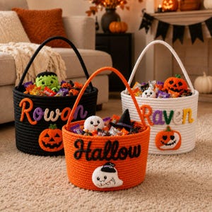 May include: Three round rope baskets for Halloween, colored black, orange, and white. Each basket features a handle, a plush toy, assorted candy, and a personalized name or word in felt lettering, including Rowan, Raven, and Hallow, with pumpkin or ghost accents.