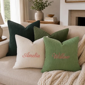 May include: Four square corduroy throw pillows in shades of dark green, olive green, and cream. The cream pillow features the embroidered name Amelia in pink, and the olive green pillow features the embroidered name Willow in pink script.