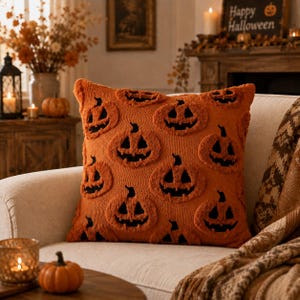 May include: A square throw pillow featuring a textured orange fabric with a repeating pattern of black jack-o'-lantern faces. The design consists of tufted pumpkin shapes with carved eyes, noses, and jagged mouths set against a solid orange background.
