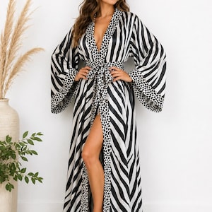 May include: A floor-length robe featuring a black and white striped pattern with a contrasting black and white spotted trim along the front opening, wide sleeves, and a matching fabric tie belt at the waist for a secure closure.