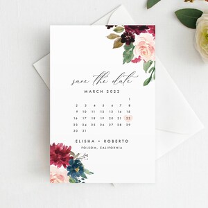 Könnte beinhalten: Save-the-Date-Karte mit einem Aquarell-Blumendesign in den Farben Burgunderrot, Rosa und Grün. Die Karte zeigt einen Kalender mit dem hervorgehobenen Datum 22. März 2022. Der Text "Save the date" ist in kursiver Schrift geschrieben. Die Namen Elisha und Roberto sind unter dem Kalender zusammen mit dem Ort Folsom, Kalifornien, gedruckt.
