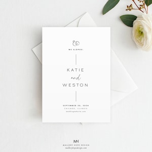 May include: A white wedding announcement card with the text "WE ELOPED!" and the names "KATIE and WESTON". The card also includes the date, location, and a website address. A white envelope and a flower are in the background.