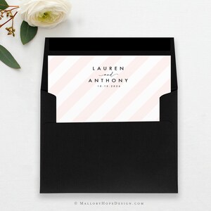 May include: A black envelope containing a light pink and white striped invitation card. The card displays the names "LAUREN and ANTHONY" and the date "10.15.2026" in black script. A white flower and greenery are in the upper left corner.