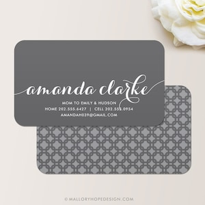 May include: Gray business card with white text. The text reads "amanda clarke" in cursive script. Below the name is the text "MOM TO EMILY & HUDSON" followed by phone numbers and an email address: "HOME 202.555.6427 | CELL 202.555.0954 AMANDAH039@GMAIL.COM".