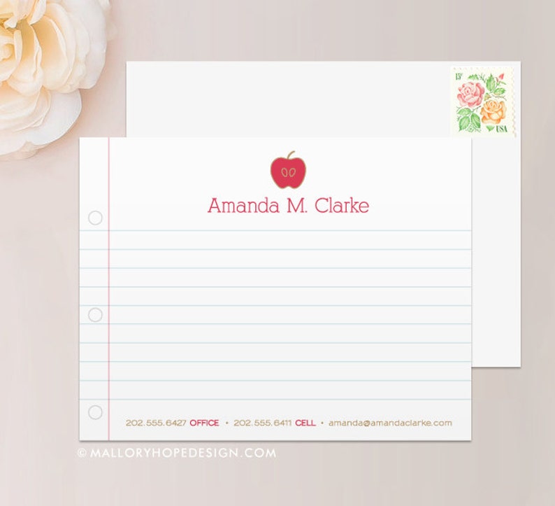 May include: A white stationery card with a red apple graphic and the name "Amanda M. Clarke" printed in red. The card has blue lines and a red border. The bottom of the card has contact information printed in black.