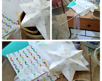 Könnte beinhalten: Ein weißer Papierstern mit geometrischer Linienkunst, einem goldenen Band und einem Holzstab mit einem weißen Band. Der Stern befindet sich in einem braunen Topf. Bunte geometrisch gemusterte Karten und andere Bastelmaterialien sind ebenfalls sichtbar.