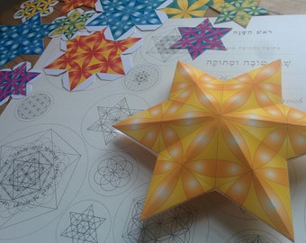 May include: A yellow, orange, and white paper star with a geometric pattern. The star is lying on a white sheet of paper with black geometric designs. The paper has Hebrew text that reads "The Light of the World" and "The Light of the World" in Hebrew.