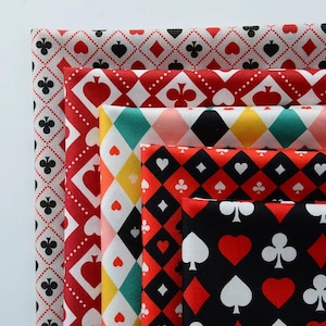 Könnte beinhalten: Ein Stapel aus fünf gefalteten Stoffmustern mit verschiedenen Spielkartenmotiven. Die Designs umfassen Rautenmuster, Herzen, Kreuz und Pik in den Farben Rot, Schwarz, Weiß, Gelb und Türkis, die in einer geschichteten Anordnung präsentiert werden.