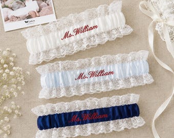 May include: Three wedding garters featuring white lace trim and a central satin band. The top garter is white, the middle is light blue, and the bottom is navy blue. Each garter is embroidered with the red text Ms. William in a script font.