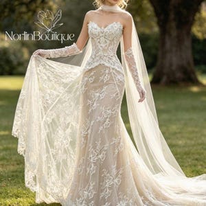 May include: A strapless ivory wedding dress featuring intricate white floral lace overlays on a nude-toned bodice and skirt. The gown includes matching lace long sleeves, a sweetheart neckline, and a long, flowing sheer veil draped from the shoulders.