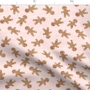 May include: A pink fabric with a repeating pattern of gingerbread men. The gingerbread men are brown with white icing and pink cheeks. The background is a light pink with white polka dots.