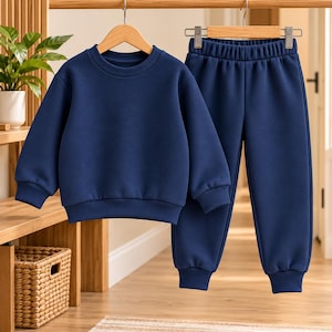 Könnte beinhalten: Ein einfarbiges, marineblaues zweiteiliges Set, bestehend aus einem langärmeligen Sweatshirt mit Rundhalsausschnitt und einer passenden Jogginghose mit elastischem Bund und Bündchen an den Knöcheln, hängend an Holzkleiderbügeln.