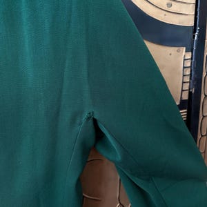 Peut inclure: Gros plan sur une manche de blazer vert fonc&eacute;. Le tissu a une texture subtile et une couture visible &agrave; l'&eacute;paule. Le blazer semble &ecirc;tre fait d'une mati&egrave;re lisse, peut-&ecirc;tre tiss&eacute;e.