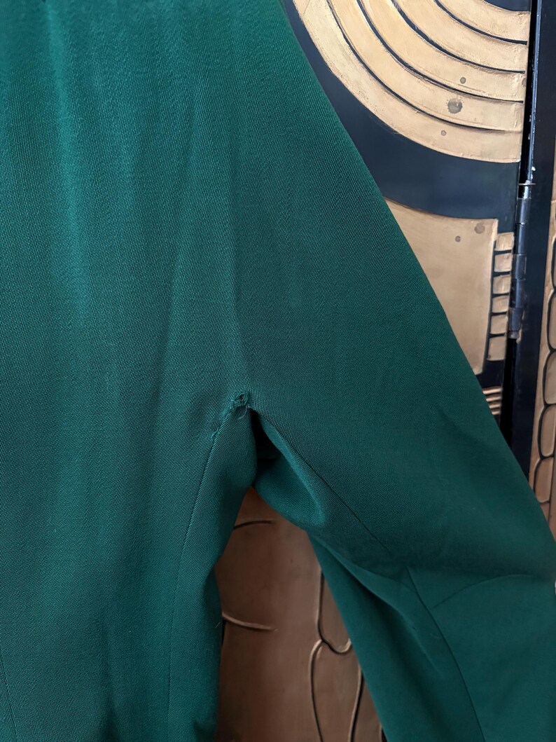 Peut inclure: Gros plan sur une manche de blazer vert fonc&eacute;. Le tissu a une texture subtile et une couture visible &agrave; l'&eacute;paule. Le blazer semble &ecirc;tre fait d'une mati&egrave;re lisse, peut-&ecirc;tre tiss&eacute;e.