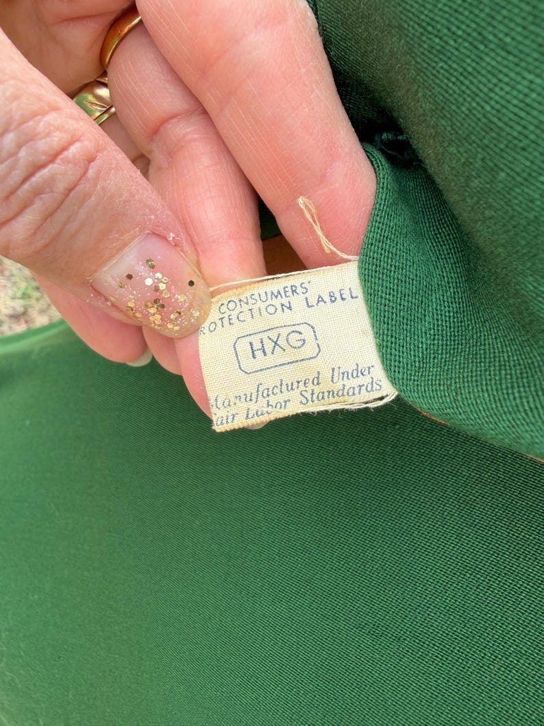 Peut inclure: Gros plan sur un tissu vert avec une &eacute;tiquette attach&eacute;e. L'&eacute;tiquette indique "CONSUMERS PROTECTION LABEL" et "Manufactured Under Fair Labor Standards". L'&eacute;tiquette porte &eacute;galement les lettres "HXG".