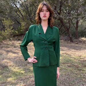 Peut inclure: Un tailleur deux pi&egrave;ces vert &eacute;meraude vintage. La veste pr&eacute;sente un design crois&eacute; avec six boutons fonc&eacute;s et un col crant&eacute;. La jupe est de style droit, longueur genou. Le costume est en tissu textur&eacute;, et le mod&egrave;le est &agrave; l'ext&eacute;rieur.