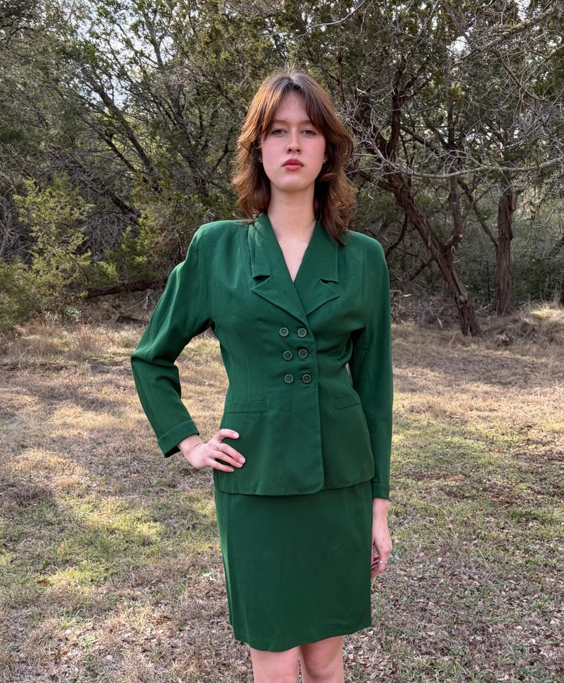 Peut inclure: Un tailleur deux pi&egrave;ces vert &eacute;meraude vintage. La veste pr&eacute;sente un design crois&eacute; avec six boutons fonc&eacute;s et un col crant&eacute;. La jupe est de style droit, longueur genou. Le costume est en tissu textur&eacute;, et le mod&egrave;le est &agrave; l'ext&eacute;rieur.