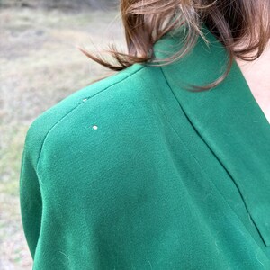 Peut inclure: Gros plan sur un blazer vert. Le blazer a un col structur&eacute; et une coupe ajust&eacute;e. Le tissu semble &ecirc;tre de couleur unie, avec une texture lisse. L'image se concentre sur l'&eacute;paule et l'encolure du v&ecirc;tement.
