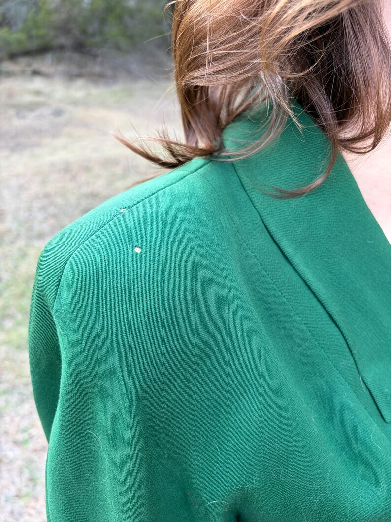 Peut inclure: Gros plan sur un blazer vert. Le blazer a un col structur&eacute; et une coupe ajust&eacute;e. Le tissu semble &ecirc;tre de couleur unie, avec une texture lisse. L'image se concentre sur l'&eacute;paule et l'encolure du v&ecirc;tement.