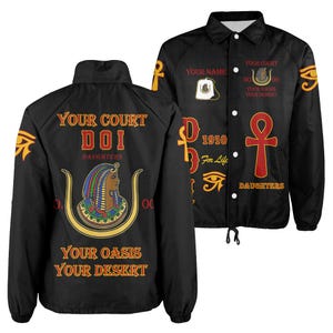May include: A black snap-front jacket featuring Egyptian-themed graphics in red, gold, and blue. The back displays a profile of a figure in a headdress with the text "YOUR COURT DOI DAUGHTERS YOUR OASIS YOUR DESERT." The front includes an ankh symbol.