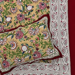 Può includere: Un set di biancheria da letto con tessuto di base color marrone chiaro e un motivo floreale in rosa, verde e blu. La federa rettangolare e il lenzuolo più grande hanno un bordo rosso scuro con finiture bianche e un motivo a melograno.