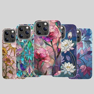 May include: Five smartphone cases featuring stained glass patterns. Designs include yellow sunflowers, a teal geometric floral motif, pink flowers on a light background, white lotus blossoms on a dark blue field, and purple leaves on a blue background.