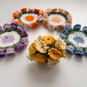 May include: Four circular crochet coasters with white centers and colorful petal-like borders in purple, orange, peach, and blue, accompanied by a small, three-dimensional yellow and cream crochet flower bouquet centerpiece.