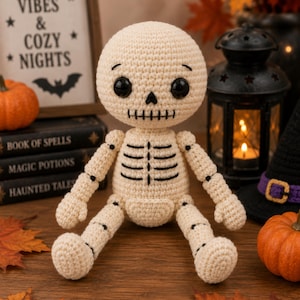 May include: A cream-colored crocheted skeleton doll with large black plastic eyes, a stitched black nose, and a stitched black mouth. The doll features black embroidered rib cage details and jointed limbs, sitting upright with a round head.