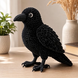 May include: A handcrafted black crochet crow figurine featuring a textured yarn body, a pointed beak, and a single visible eye with a white scalloped iris. The bird stands on two detailed crochet legs with pointed black claws, showcasing intricate stitching.
