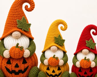 May include: Three crocheted gnomes of varying sizes, each wearing a tall, curled hat in orange, yellow, or red with a green leaf accent. Each gnome has a white beard, beige nose, green sleeves, and holds a small pumpkin atop a pumpkin-shaped base.