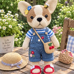 Op de afbeelding: Een gehaakte Franse bulldog pop van bruin en crèmekleurig garen, gekleed in een blauw-wit gestreept shirt, een blauwe tuinbroek in spijkerstofstijl met bloemenborduursel, een beige schoudertasje met kersen en rode sandalen met witte bloemen.