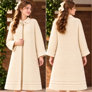May include: A cream-coloured, long-sleeved, knee-length knit coat featuring a textured stitch pattern, a classic collar with a small tie closure at the neckline, and wide cuffs. The garment is shown from both the front and back views.