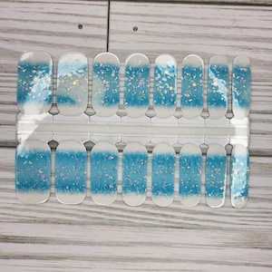 May include: A sheet of nail wraps featuring a blue and white watercolor design with iridescent glitter accents. The nail wraps are arranged in a grid, ready for application. The design resembles a dreamy, aquatic theme.