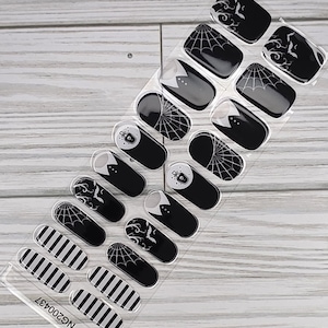 May include: A sheet of Halloween-themed nail art stickers. Designs include black and white stripes, spiderwebs, bats, and ghost images. The stickers are on a clear backing with the code NG200437.