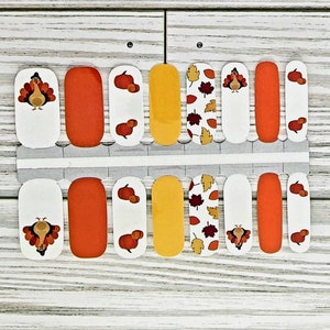 May include: A set of 10 nail wraps featuring a Thanksgiving theme. The wraps include images of turkeys, pumpkins, and autumn leaves in shades of orange, yellow, and brown.