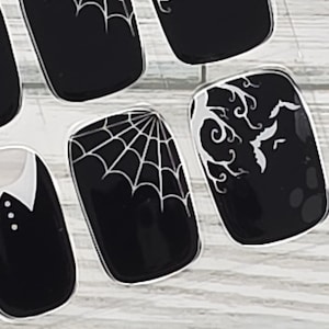 May include: Black nail art with white spiderwebs, bats, and decorative swirls. The nail designs are on a clear background, perfect for Halloween or gothic-themed looks. The nails are rectangular in shape.