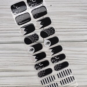 May include: A sheet of black and white nail wraps with various Halloween-themed designs. The designs include bats, spiderwebs, and stripes. The nail wraps are in a clear plastic package with the text "NG200437".
