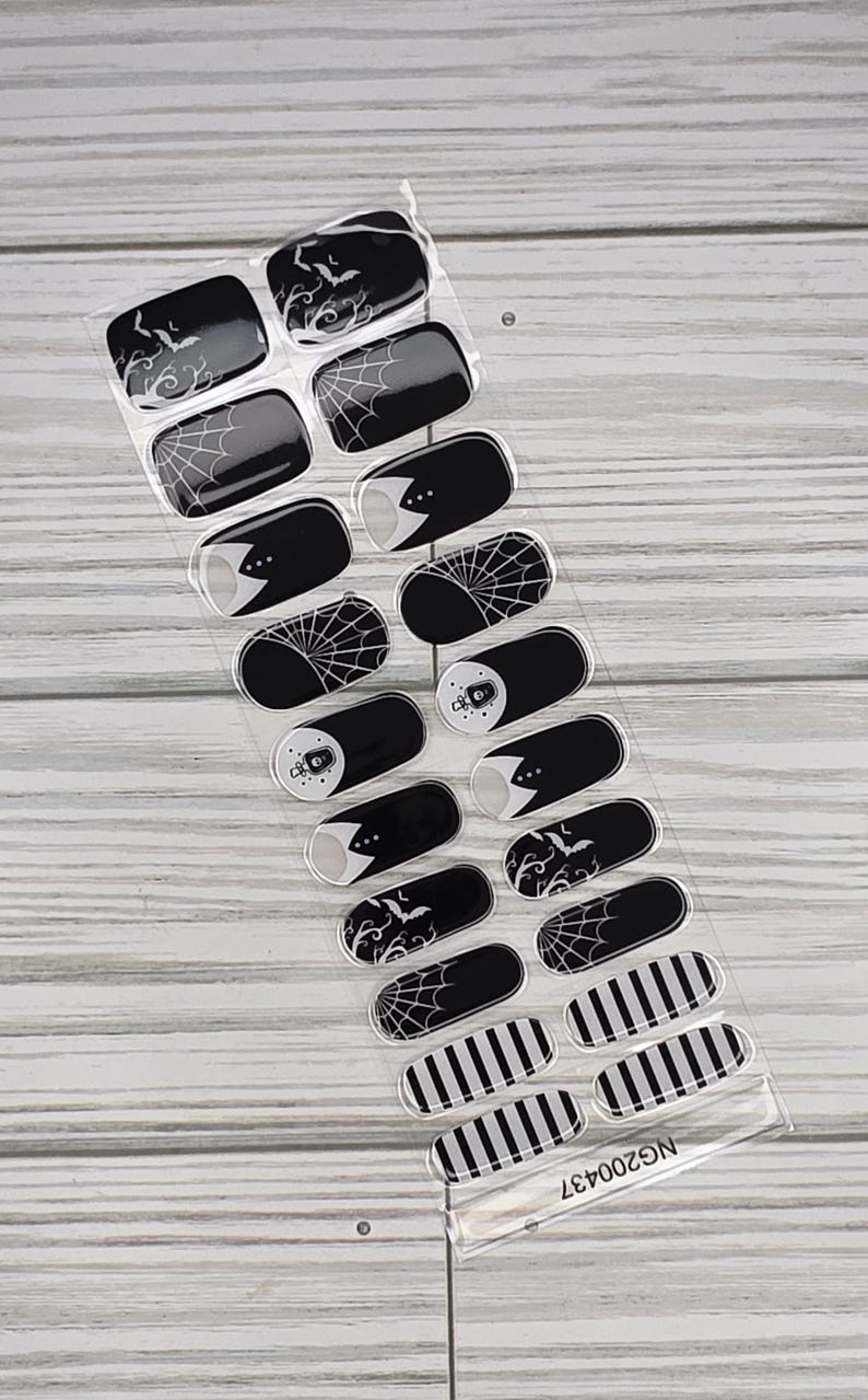 May include: A sheet of black and white nail wraps with various Halloween-themed designs. The designs include bats, spiderwebs, and stripes. The nail wraps are in a clear plastic package with the text "NG200437".