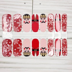 May include: Set of 10 nail wraps featuring a red and white snowflake design with a nutcracker soldier illustration. The nail wraps are in a clear plastic sheet.