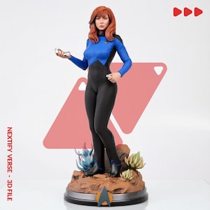 Peut inclure: Une figurine debout représentant une personne aux cheveux auburn mi-longs, vêtue d'un uniforme bleu et noir avec un insigne doré. Le personnage tient un petit appareil argenté sur un socle rocheux avec des plantes et un emblème delta.