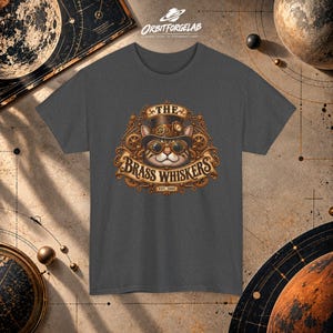 May include: A charcoal gray t-shirt featuring a graphic of a cat wearing a top hat and goggles, surrounded by brass-colored gears and scrollwork. The text reads THE BRASS WHISKERS EST. 1888 in a decorative font centered on the chest.