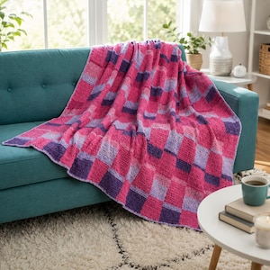 Peut inclure: Un plaid crocheté présentant un motif à carreaux répétitif dans des tons de rose vif, violet clair et violet foncé. Le textile possède une construction texturée à base de fil avec des carrés visibles disposés en grille sur la surface.