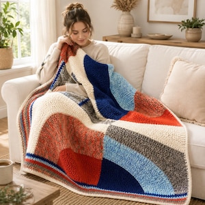 May include: A crochet blanket featuring a geometric pattern of large curved shapes and blocks in cream, navy blue, bright orange, light blue, and textured grey yarn. The blanket has a thick, soft, and chunky knit texture with visible stitches.