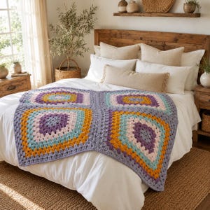 May include: A crochet blanket featuring a repeating square pattern in shades of purple, light blue, mustard yellow, and cream. The blanket is constructed from interconnected granny squares with a textured yarn finish, draped over a white bedspread.